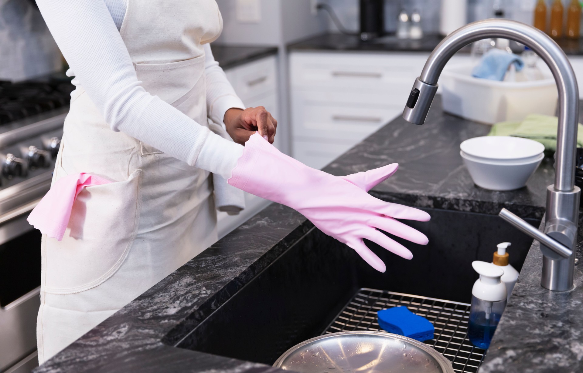 Housekeeper at kitchen sink putting on glove